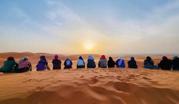 People sitting on a sand dune watching a desert sunset.