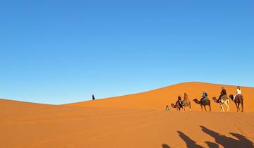 Group of people riding camels on sand dunes in the desert.