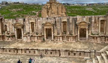 Ancient Roman amphitheatre with green hills and ruins in the background.