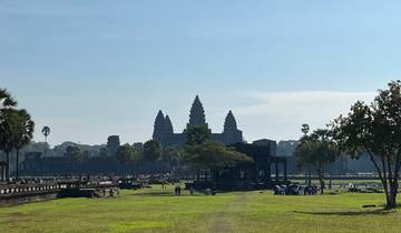 View of Angkor Wat with grass and trees in the foreground.