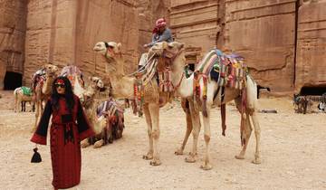 Woman posing next to camels in front of a rock-cut structure.