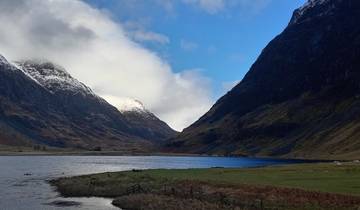 A scenic view of a lake surrounded by snow-capped mountains under a blue sky.