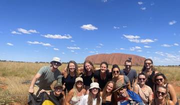 Group of people posing with Uluru in the background.