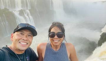 Couple smiling in front of a large waterfall.