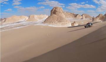Jeep driving on sand dunes in a desert landscape.