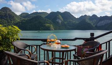 Table with pastries and drinks overlooking a scenic bay with karst mountains.