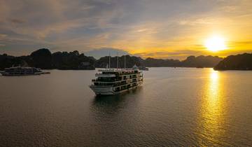 Cruise ship on water at sunset surrounded by karst mountains.