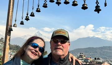 A couple posing with bells and mountains in the background.