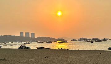 Beach scene at sunset with boats on the water and people on the shore.