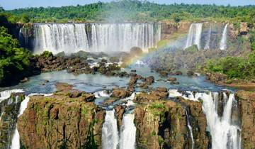 Grand waterfall with rainbow over lush forest.