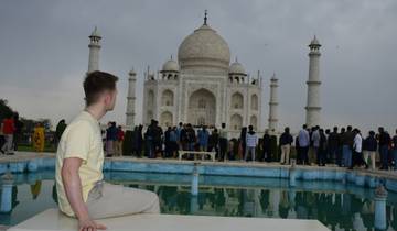 Man sitting and admiring the Taj Mahal with a pool in front.