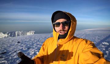 Man in a bright yellow jacket standing on a snowy mountain.