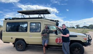 Two men posing with a safari vehicle under a blue sky.