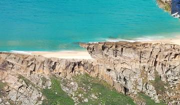 Cliff with a sandy beach and clear blue water.