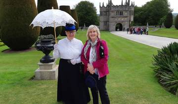 Two women pose in historical costumes in front of an old stone building