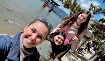 Three people smiling with Japanese torii gate by the sea.