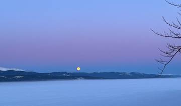 Moonrise over a mountain range with a colorful evening sky.