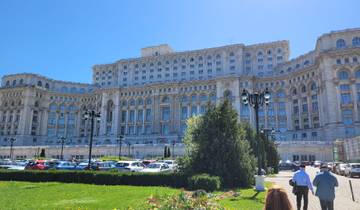 The massive Palace of the Parliament with green gardens below under a bright sky.