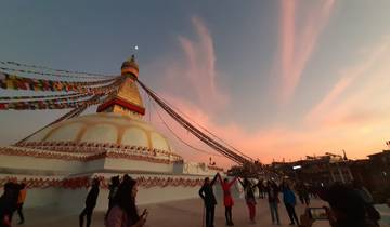 A large stupa with prayer flags during sunset, people around.