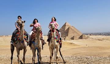 Tourists riding camels with pyramids in the background.