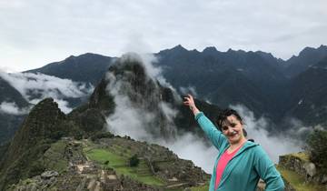 Person pointing at Machu Picchu with mountains and mist in the background.