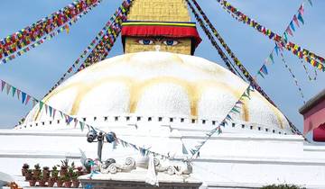 Large white stupa with prayer flags and eyes painted on it.