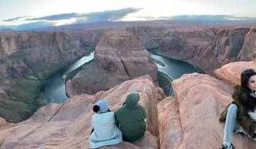 People sitting on the edge of a canyon with a river below.