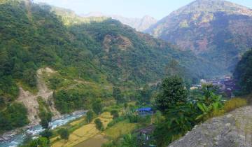 A scenic view of a valley with a river, fields, and houses, surrounded by mountains.