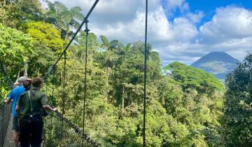 Tourists on a hanging bridge in a tropical setting with a volcano.