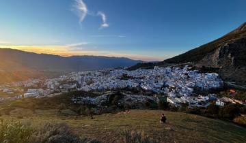 Hilltop view of a blue city with sunset in the background.
