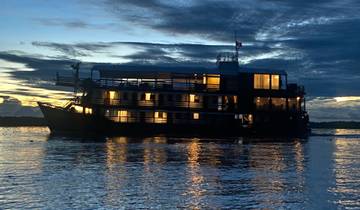 A boat with lit windows on a river at dusk.