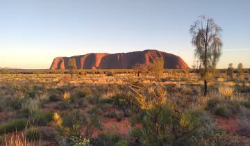 Uluru rock formation at sunset in a desert landscape.