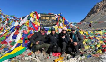 Group of trekkers posing at Thorong La pass, surrounded by flags.
