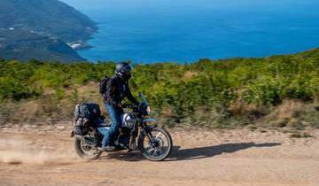 Person riding a motorcycle on a dirt road with sea in the background.
