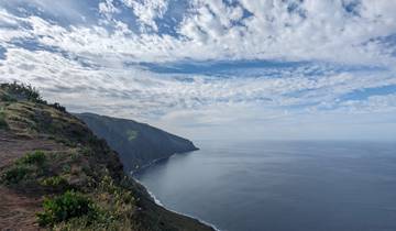 Cliffside overlooking vast ocean with cloudy sky.