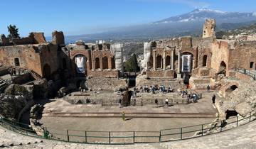 Ancient ruins of an amphitheater with mountains in the background.