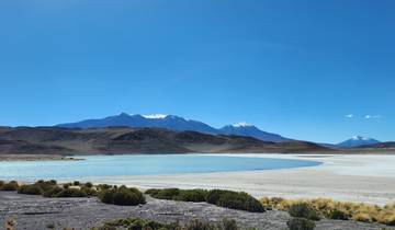 Turquoise lagoon with mountains in the background under a clear sky.