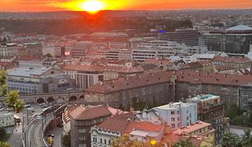 Cityscape at sunset with red tile roofs and distant hills.
