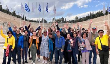 Group of people posing with Greek flags in the background.