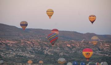 Hot air balloons floating over a scenic valley at sunrise.