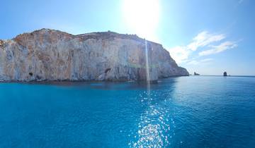 Rocky coastal cliffs with bright sunlight reflecting on the water.
