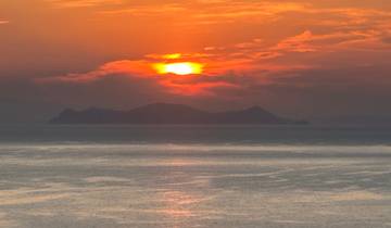 Sunset over the sea with an island silhouette.