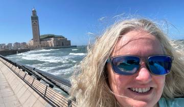 Person taking a selfie near a waterfront with a large mosque in the background.