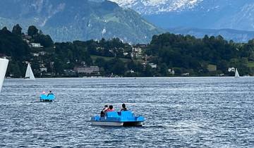 Paddle boats with people on a lake surrounded by mountains.