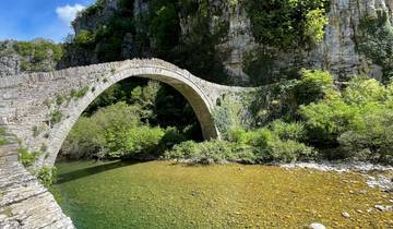 Stone arch bridge over a clear river surrounded by lush vegetation.