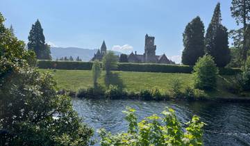A historic building by a river with mountains in the background.