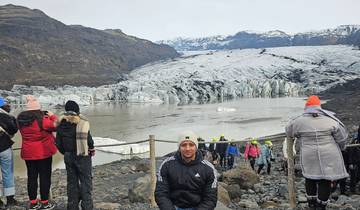 Tourists exploring a glacier with a large body of water and mountains in the background.