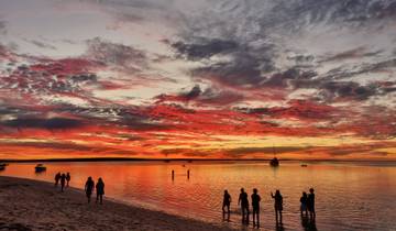 People enjoying a vibrant sunset by the sea with a dramatic sky filled with colorful clouds.