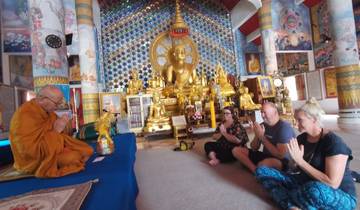 Monk leading a ceremony with people praying in a decorated temple.
