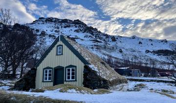 A small house with a grassy roof in a snowy landscape.
